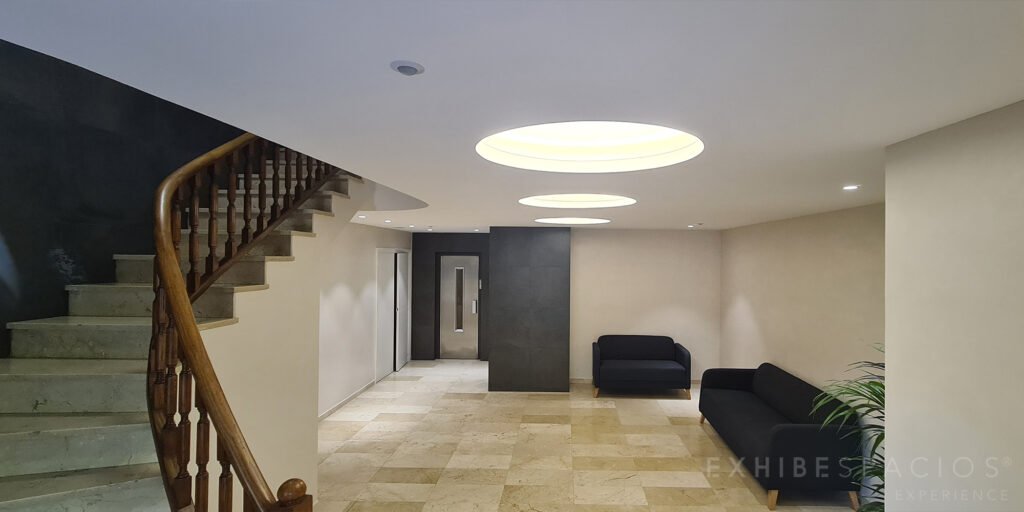 Reforma de vestíbulo y escalera en Passeig Maragall, Horta-Guinardó: techo a doble altura con tres círculos acampanado de luz indirecta y escalera en curva y microcemento en las paredes
